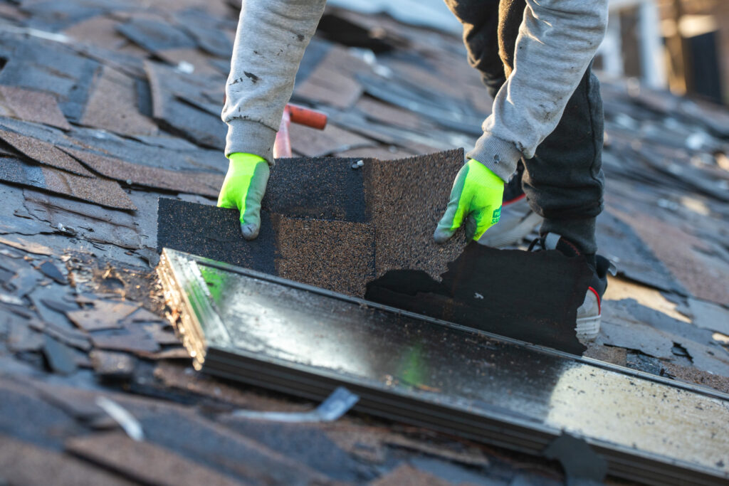 man pulling up shingles on a roof