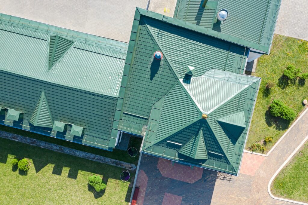 green metal shingled house roof top with installed ventilation pipes. aerial view