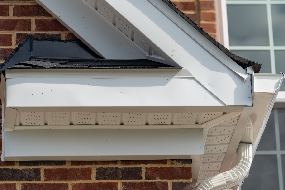 Gable with brick and vinyl siding, white frame gutter guard system, fascia, drip edge, soffit, on a pitched roof attic