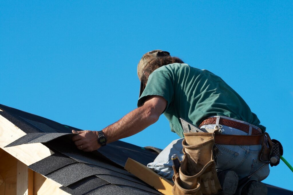 worker on roof putting shingles down