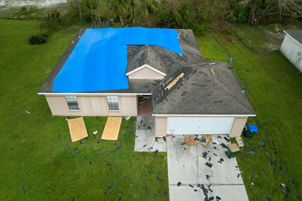 Top view of leaking house roof covered with protective tarp sheets against rain water leaks until replacement of asphalt shingles. Damage of building rooftop as aftermath of hurricane Ian in Florida.