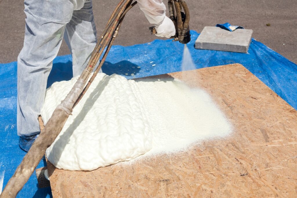 Close up view of technician dressed in a protective white uniform spraying foam insulation 