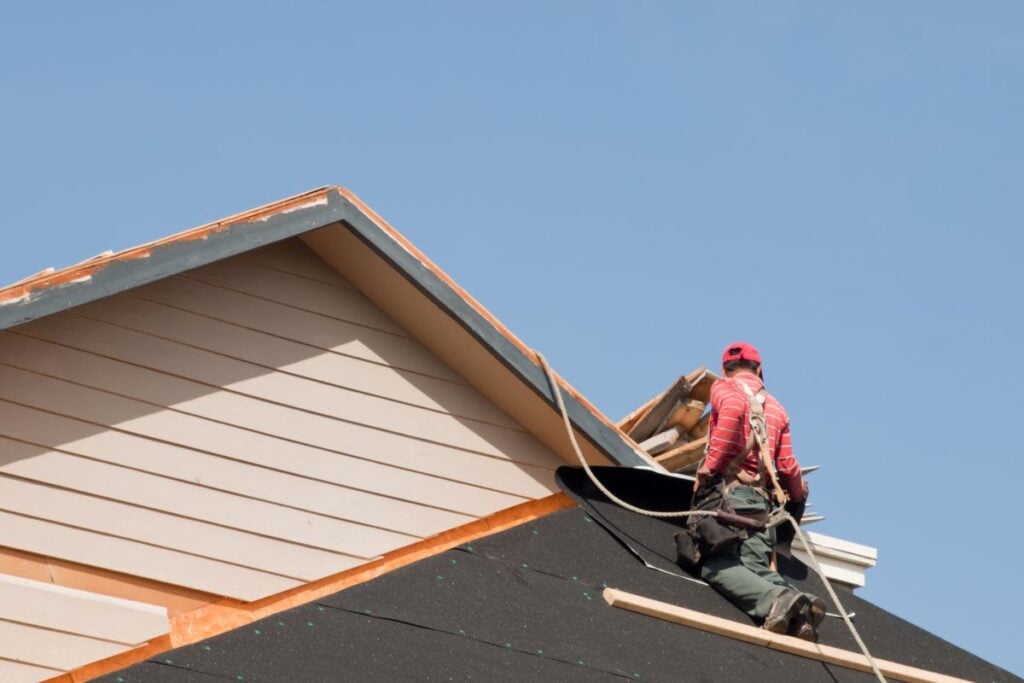 DIY roof replacement worker using safety equipment replacing new shingles