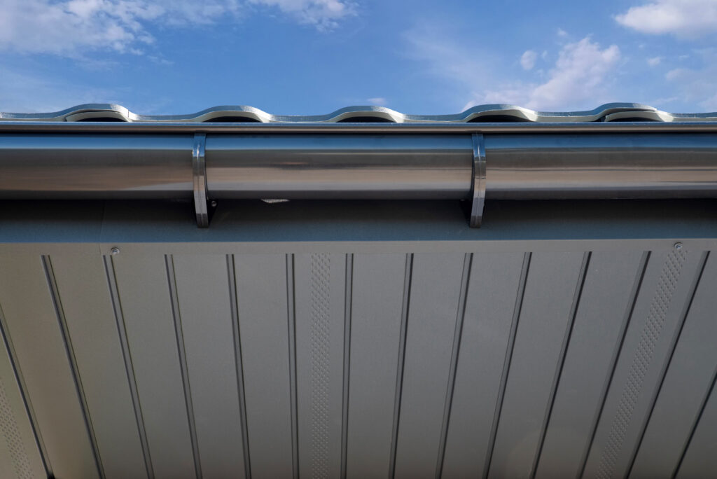 A sleek gray metal roof with integrated gutters under a blue sky