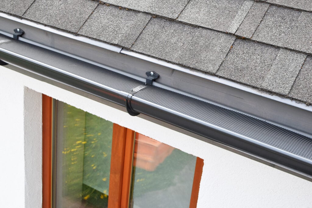 Close-up of a seamless gutter with a gutter guard installed along the edge of a shingle roof