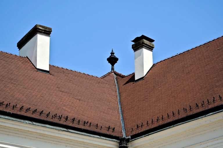 white stucco finished chimney. sloped roof with red brown clay roof tiles. metal roof flashing.