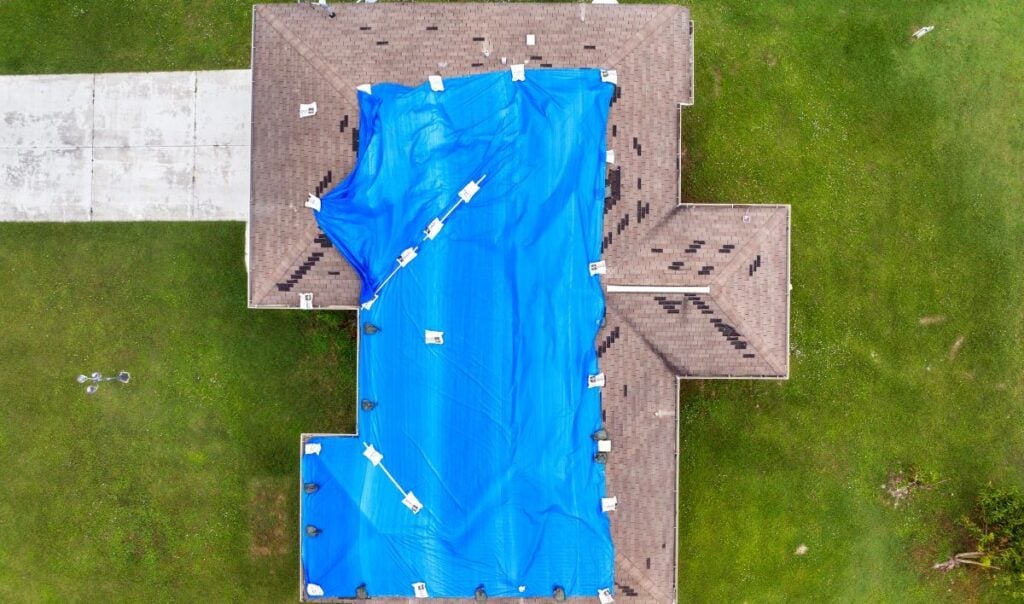 a hurricane affected house roof covered by a blue tarp