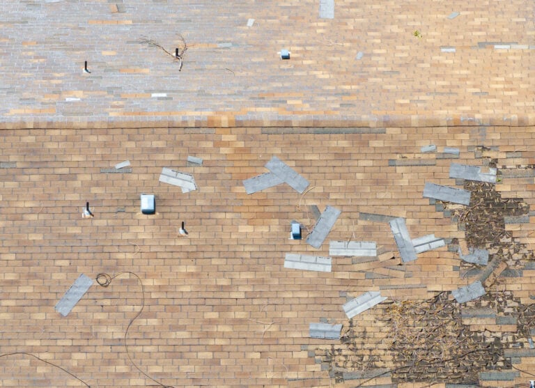 storm damage roof repair Aerial view reveals a damaged roof. Shingles blown off during a storm and scattered. Structure requires urgent repair. Ideal for insurance or construction contexts