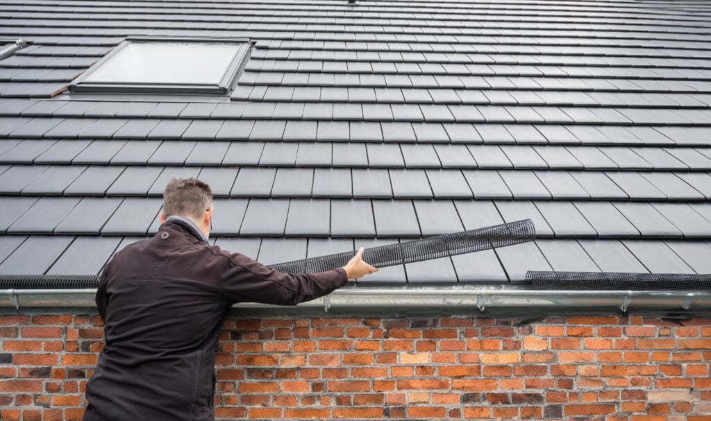 gutter guard installation Man puts a gutter mesh to the rain gutter to protect the gutter from leaves.