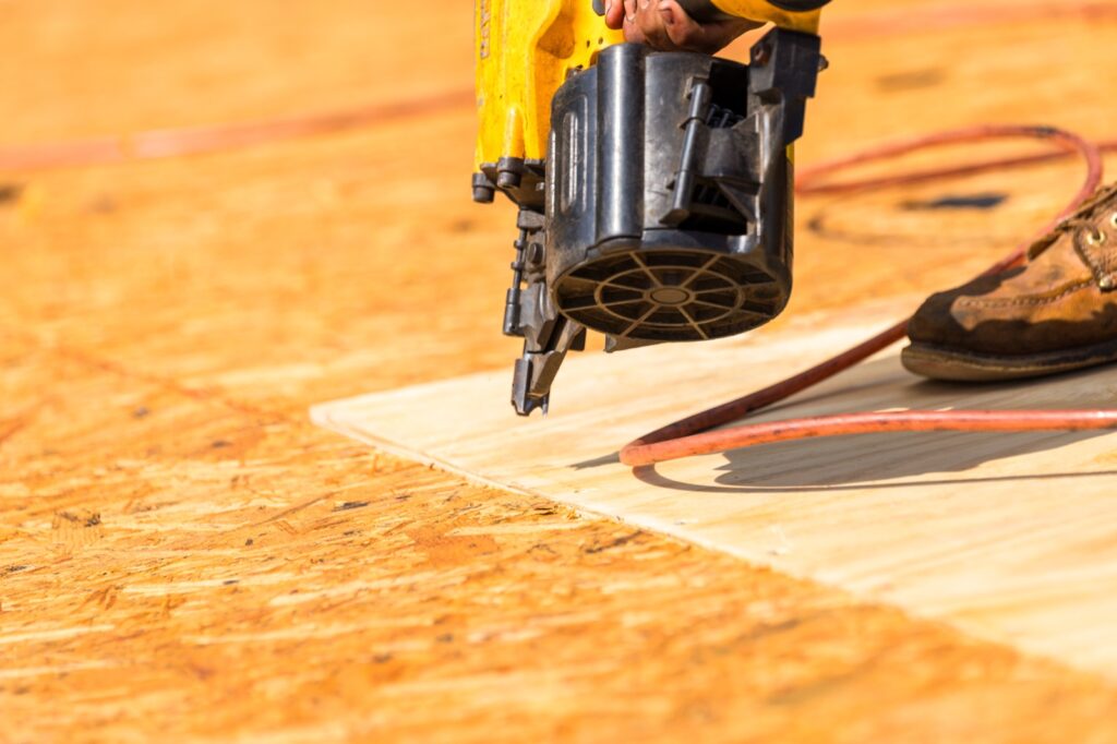 Pneumatic nail gun fastening a new plywood roof deck panel on a Pensacola home