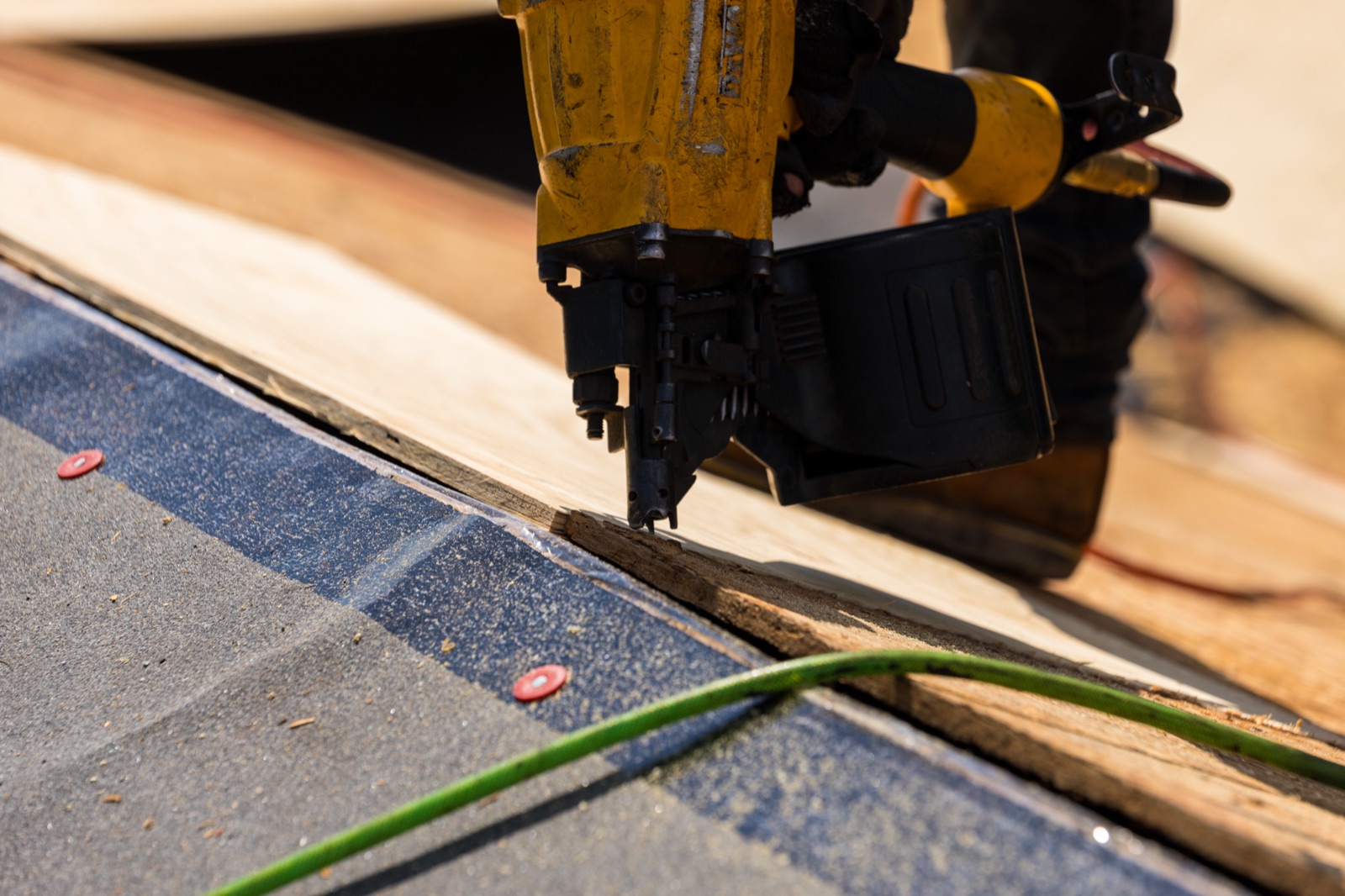 Roofer fastening new decking at the roof edge over synthetic underlayment with cap nails on a Pensacola roof replacement