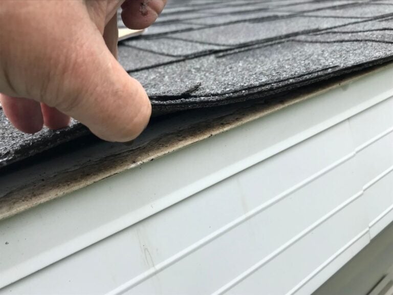guy's hand lifting shingles roof